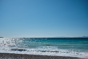 sunny day on the beach with waves in the background and a windsurfer in the background