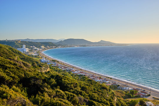 beautiful view of the sea with resort and mountains in the background and green bushes in the foreground