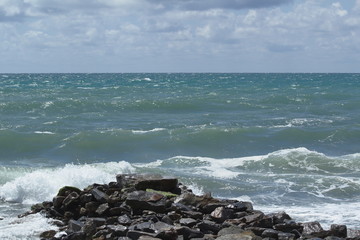 sea waves running on a stone Cape against the sky with white clouds