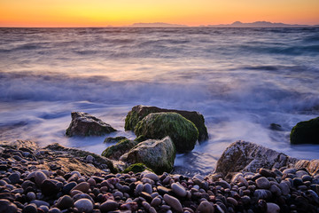 Obraz premium Stone beach in the foreground and large stones with moss in the sea with mountains and sunset in the background