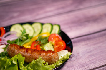 Beautiful grilled sausages on a black plate with vegetables and a background of boards.