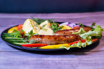 Beautiful grilled sausages on a black plate with vegetables and a background of boards.