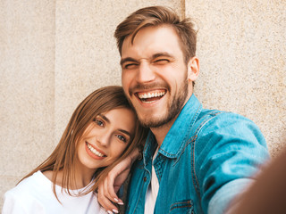 Smiling beautiful girl and her handsome boyfriend in casual summer clothes. Happy family taking selfie self portrait of themselves on smartphone camera. Having fun on the street background