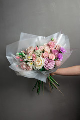 A beautiful wedding bouquet of flowers, fresh roses of different colors, in the hands of a girl, against a gray wall