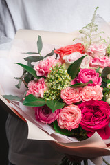 A beautiful wedding bouquet of flowers, fresh roses of different colors, in the hands of a girl, against a gray wall