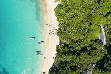 View from above, stunning aerial view of a beautiful tropical beach with white sand and turquoise clear water, long tail boats and people sunbathing, Banana beach, Phuket, Thailand.
