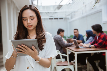 asian female worker using tablet pc with partner in the background