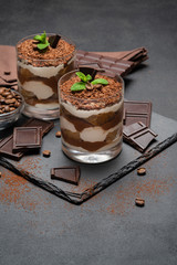 Classic tiramisu dessert in a glass and pieces of chocolate on dark concrete background