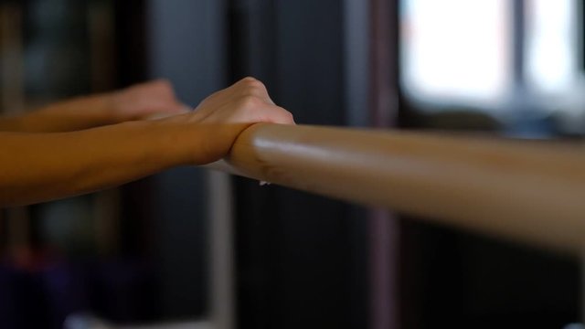 girl professional dancer nice hands hold ballet barre wooden handrail in front of mirror close view slow motion.