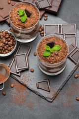 Classic tiramisu dessert in a glass and pieces of chocolate on dark concrete background