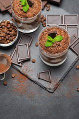 Classic tiramisu dessert in a glass and pieces of chocolate on dark concrete background