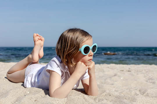 Funny little girl (7 years old) in sunglasses lies on the beach.