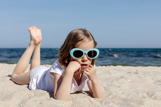 Funny little girl (7 years old) in sunglasses lies on the beach.