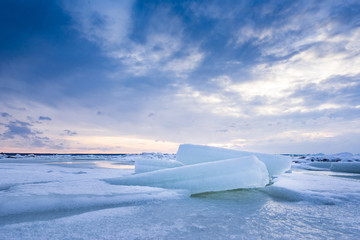 Fototapeta na wymiar Beach in wintertime. Frozen sea, evening light and icy weather on shore like fairy tale country. Winter on coast. Blue sky, white snow, ice covers the land.