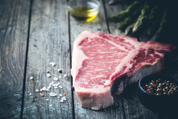 Raw T-bone Steak with fresh herbs and oil on dark wooden background