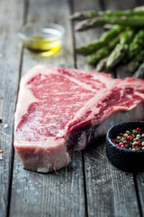 Raw T-bone Steak with fresh herbs and oil on dark wooden background