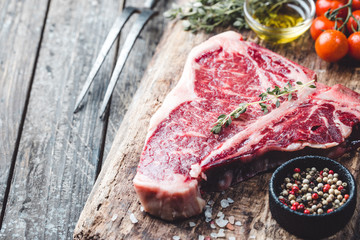 Raw T-bone Steak with fresh herbs and oil on dark wooden background