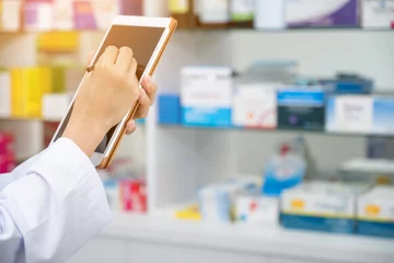 Papier Peint photo Pharmacie Pharmacien travaillant avec un ordinateur tablette dans la pharmacie le tenant dans sa main tout en lisant des informations