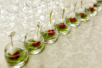 the buffet at the reception. Glasses of wine and champagne on background. Assortment of canapes in glass cups. Banquet service. Catering food, snacks with cheese and small tomatoes