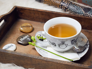 a didgeridoo and a wooden tablet with a filled teacup on it. Decorated with a flower and three labeled pebbles, Healing, Relax, Emotions. View 1