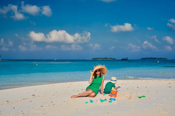 Fototapeta na wymiar Woman in green dress with three year old boy on beach
