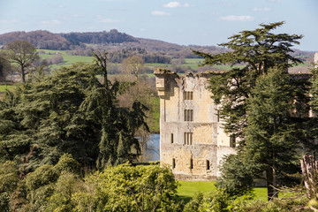 Fototapeta na wymiar Wardour Castle, near Salibsury in Wiltshire, framed by trees on a bright sunny spring day and surrounded by lush green English countryside hills and farmland