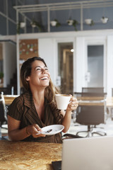 Vertical shot successful carefree girlfriend meet boyfriend lunch drink coffee laughing out loud joyfully raise head up hold cup coffee giggling cheerful near opened laptop visit co-working cafe