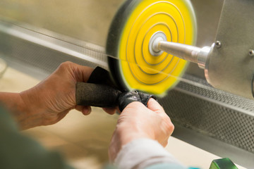 Hands of the jeweler polishes silver jewelry brooch on the polishing wheel