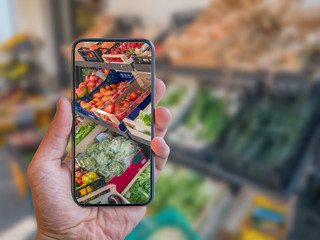 Augmented reality grocery shopping mobile app. Hand is holding cellphone with AR application scanning vegetables at food market.