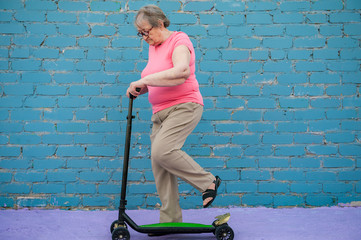 Fototapeta na wymiar elderly woman in pink T-shirt and glasses is learning to ride new scooter. concept of an active lifestyle, sports