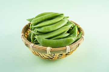Fresh bamboo pod vegetable sweet bean poster background material in a bamboo sieve on light green...