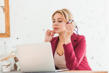 Beautiful clever business woman sitting at the table at workstation with laptop