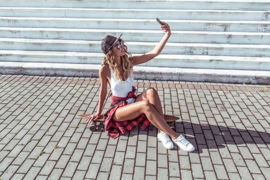 Woman summer city white body. Skate board Beautiful slim figure, sunglasses sneakers. Photographs phone online video call application happy smiling. Concept fashion style modern lifestyle. Free space.