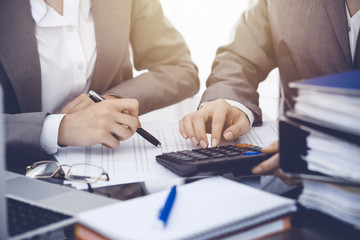 Two female accountants counting on calculator income for tax form completion hands close-up. Business and audit concept