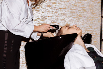 Gorgeous cute young woman enjoying head massage while professional hairdresser applying shampoo her hair. Close up of hairdresser's hands washing hair to the client.