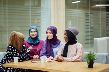 Group of beautiful young muslim business women wearing hijabs of different colour, are sharing...