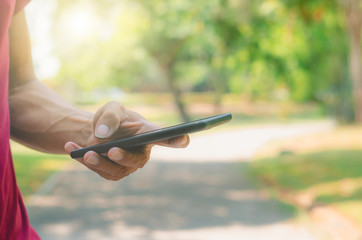 close up handsome man use left hand typing mobile phones and touch screen working with app devices in park with sunrise and green blur nature background.