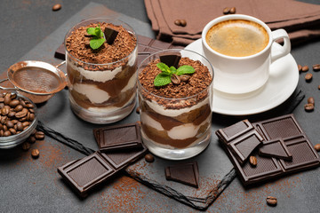 Classic tiramisu dessert in a glass and cup of coffee on dark concrete background