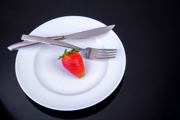 empty plate with knife and fork an one lonely strawberry