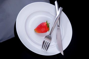 lonely strawberry on a white plate with cutlery as diet plan