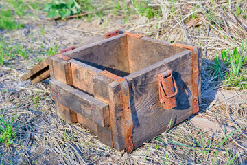 An antique wooden box with rusty metal hardware fittings rests on a grass background.