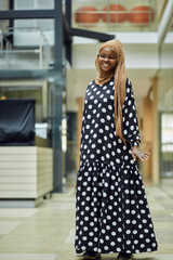 Smiling young islamic African woman wearing fashionable headscarf and dress standing on a metro train station with a bag in her hand