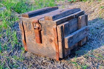 An antique wooden box with rusty metal hardware fittings rests on a grass background.