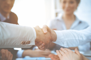 Business people shaking hands at meeting while theirs colleagues clapping and applauding. Group of...
