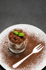 Classic tiramisu dessert in a glass on plate with fork silhouette on dark concrete background