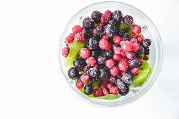Flat lay of a blender and fresh seasonal berries and fruits over white background, preparing smoothies, detox, healthy clean eating. Summer drinks.