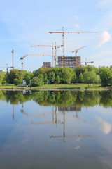 Construction of residential buildings with cranes against the blue sky in the early morning and reflected in the pond