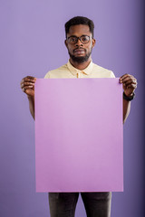 Picture of young african american man holding blank board on violet background