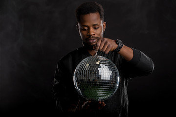 Fototapeta na wymiar Young cool black man with disco ball over black background
