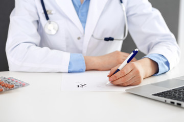 Female doctor filling up prescription form while sitting at the desk in hospital closeup.  Healthcare, insurance and excellent service in medicine concept 